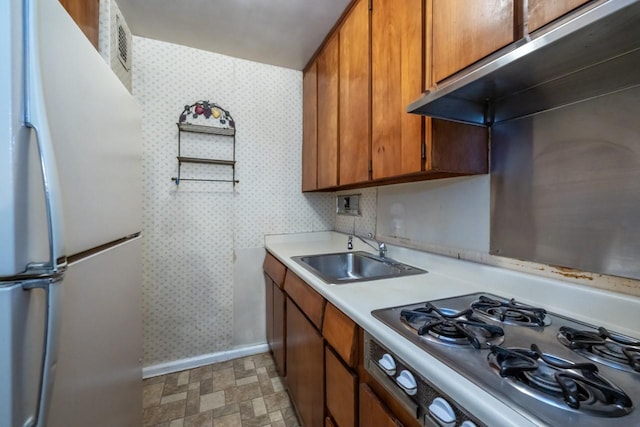 kitchen with stainless steel gas cooktop, a sink, freestanding refrigerator, and wallpapered walls