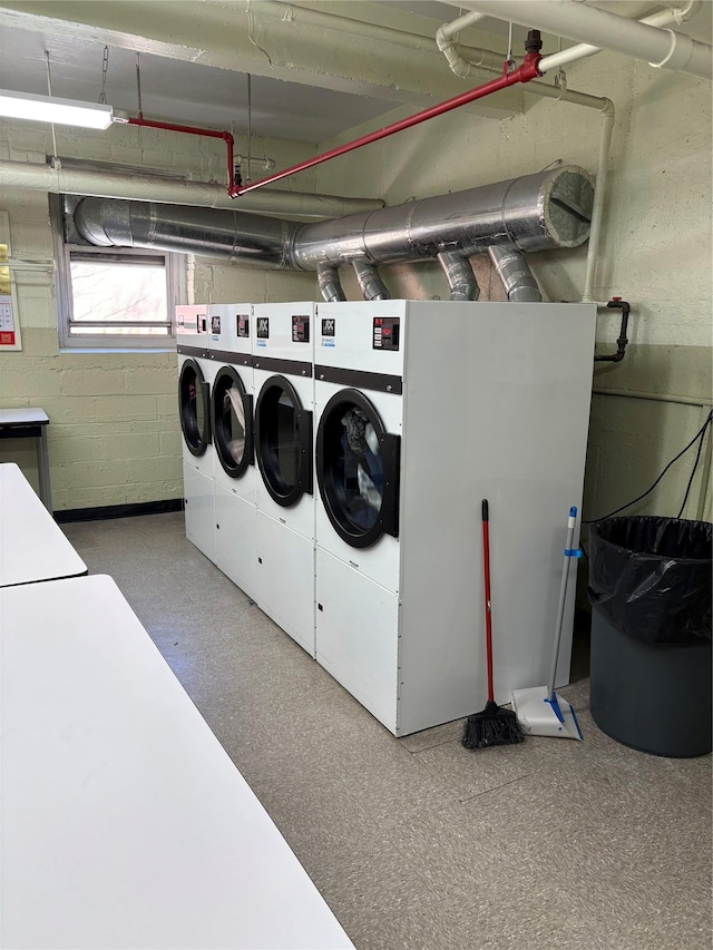 common laundry area with concrete block wall, washing machine and clothes dryer, and tile patterned floors