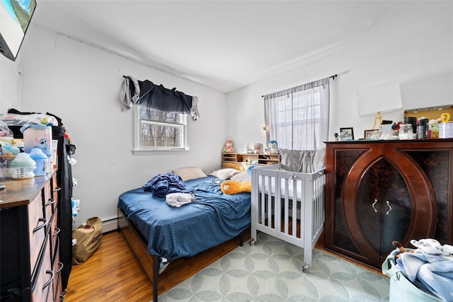 bedroom featuring multiple windows, baseboard heating, and wood finished floors