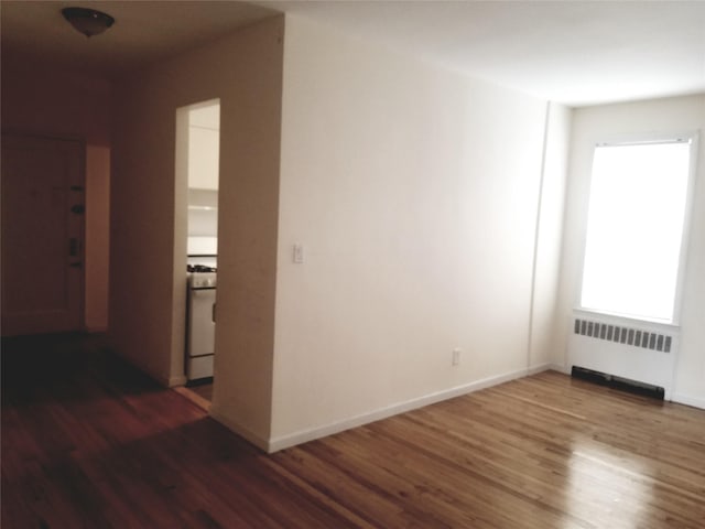 empty room with baseboards, wood finished floors, and radiator