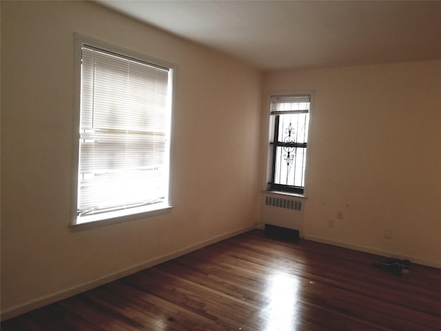 empty room with radiator heating unit, wood finished floors, and baseboards