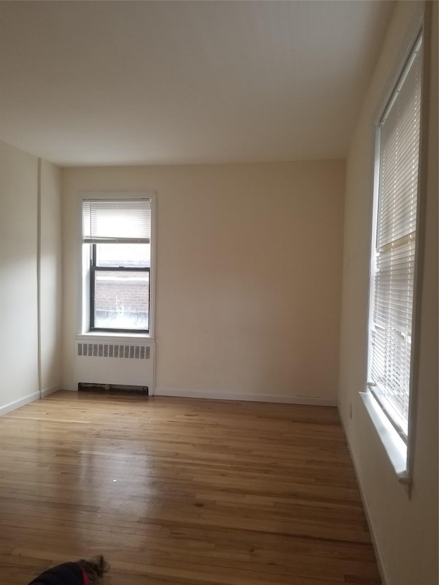 unfurnished room with baseboards, plenty of natural light, light wood-style flooring, and radiator heating unit