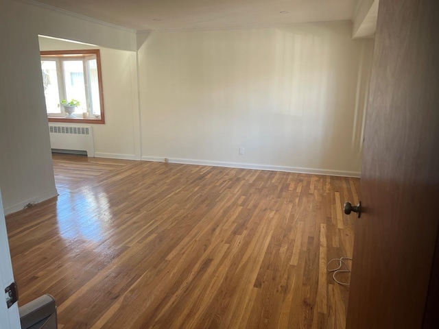 spare room featuring baseboards, crown molding, radiator heating unit, and wood finished floors