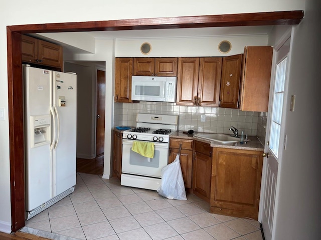 kitchen featuring light tile patterned flooring, white appliances, a sink, brown cabinets, and tasteful backsplash