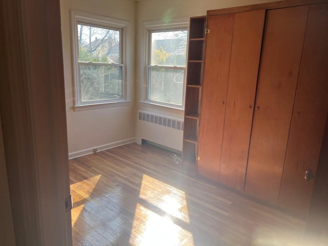 unfurnished bedroom with baseboards, a closet, light wood-type flooring, and radiator