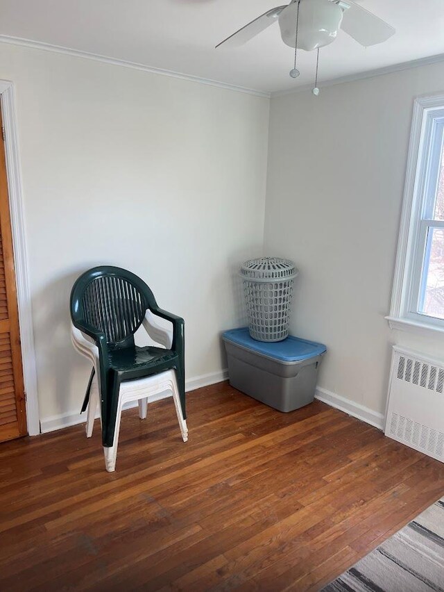 sitting room featuring wood finished floors, a ceiling fan, baseboards, ornamental molding, and radiator