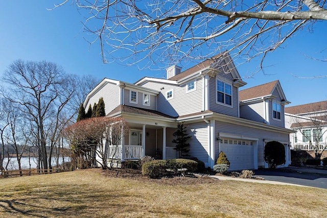 view of front of home with a chimney, covered porch, an attached garage, driveway, and a front lawn