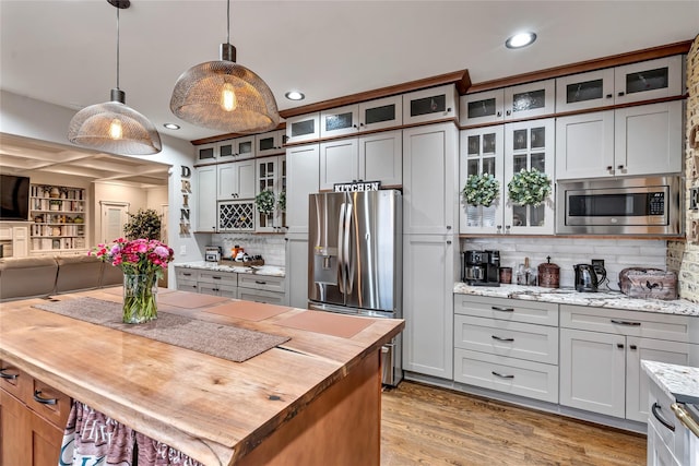 kitchen with open floor plan, stainless steel appliances, light wood-style floors, pendant lighting, and wooden counters