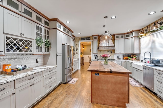 kitchen with a center island, appliances with stainless steel finishes, light wood-style floors, a sink, and wood counters