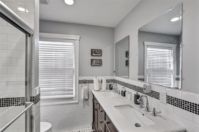 bathroom with toilet, a shower stall, tile walls, and a sink