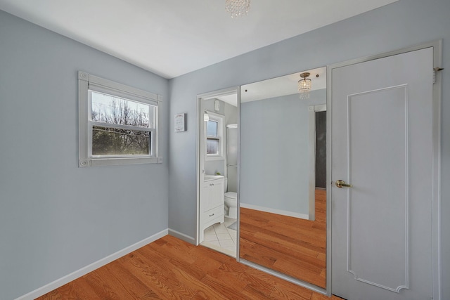 unfurnished bedroom featuring light wood finished floors, connected bathroom, and baseboards