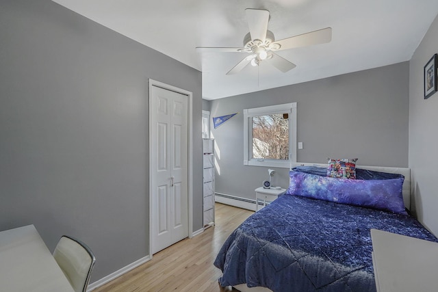 bedroom featuring a baseboard heating unit, light wood-type flooring, baseboards, and a ceiling fan