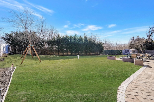 view of yard with a fenced backyard, an outbuilding, a playground, and a patio