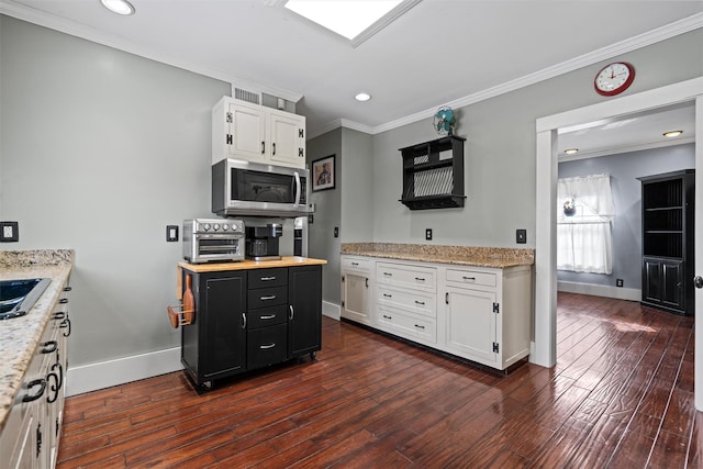 kitchen featuring white cabinetry, dark cabinetry, stainless steel microwave, and crown molding