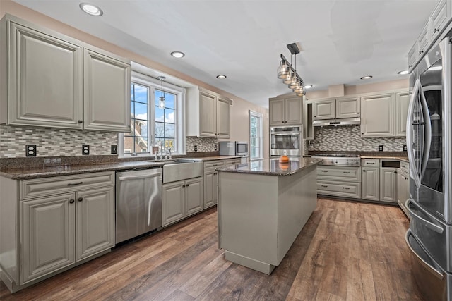 kitchen featuring a center island, pendant lighting, stainless steel appliances, wood finished floors, and under cabinet range hood