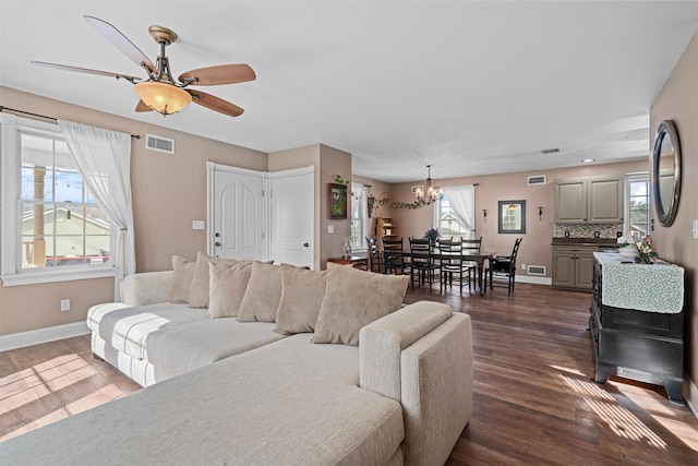 living room with dark wood-style flooring, visible vents, baseboards, and ceiling fan with notable chandelier