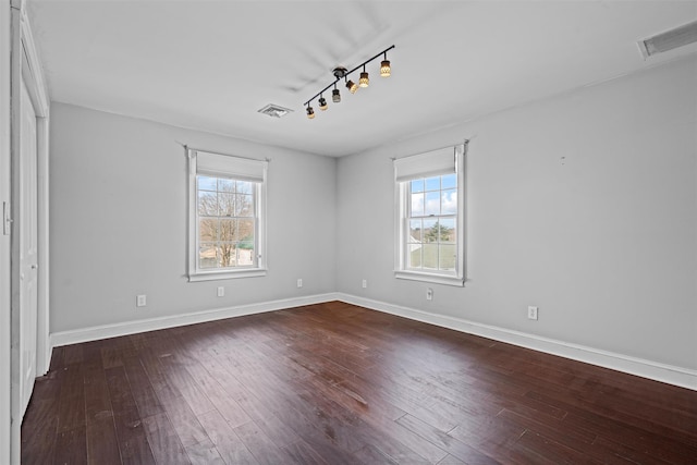 empty room featuring dark wood-style flooring, visible vents, and baseboards