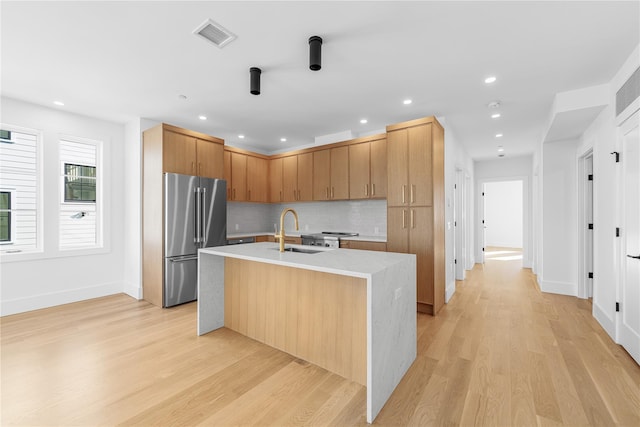 kitchen with a sink, light wood finished floors, decorative backsplash, and high end fridge