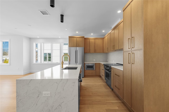 kitchen with light wood finished floors, an island with sink, high quality appliances, backsplash, and a sink