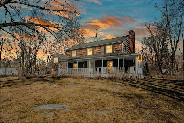 view of front of property with a porch, a chimney, and a yard