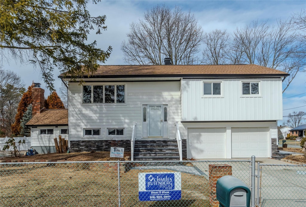 raised ranch with a fenced front yard, a gate, driveway, and a garage