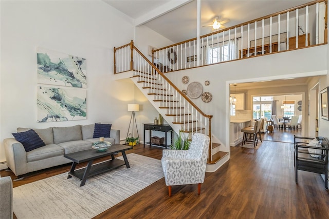 living room with beam ceiling, stairway, a high ceiling, a ceiling fan, and wood finished floors