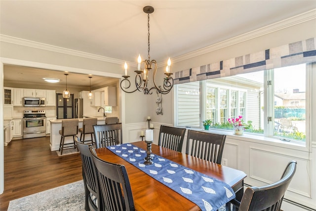 dining room with dark wood finished floors, a wainscoted wall, ornamental molding, a chandelier, and a decorative wall