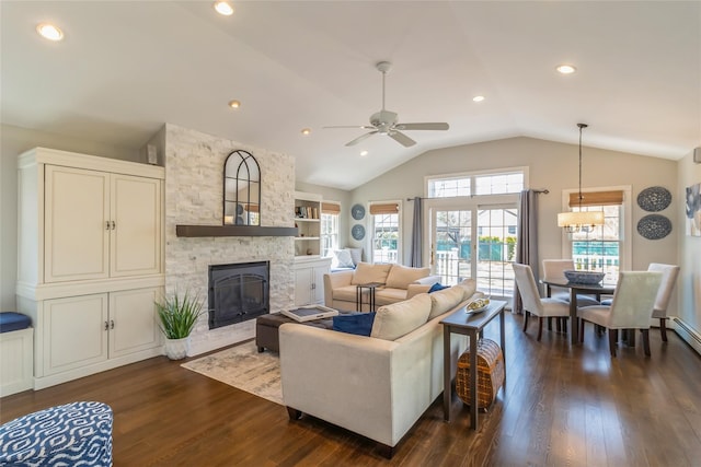 living room with vaulted ceiling, ceiling fan, a stone fireplace, and dark wood-style flooring