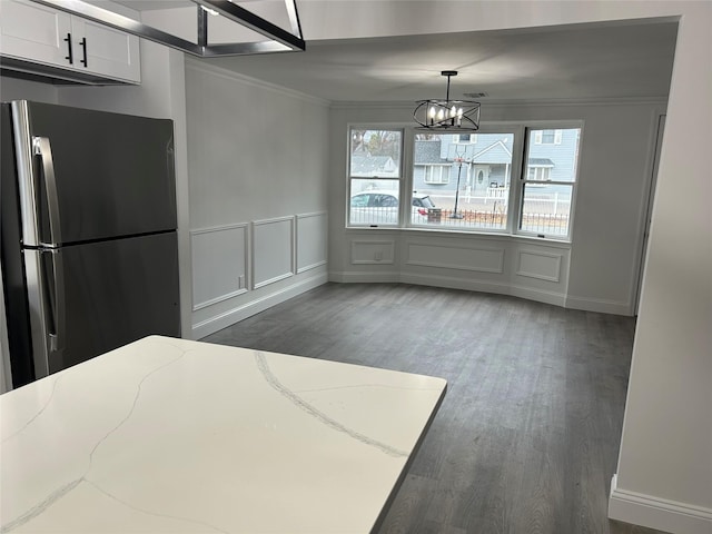 unfurnished dining area featuring a notable chandelier, ornamental molding, wood finished floors, and a decorative wall