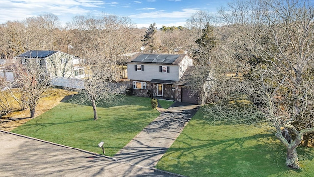 view of front facade with solar panels, a front yard, a garage, stone siding, and driveway