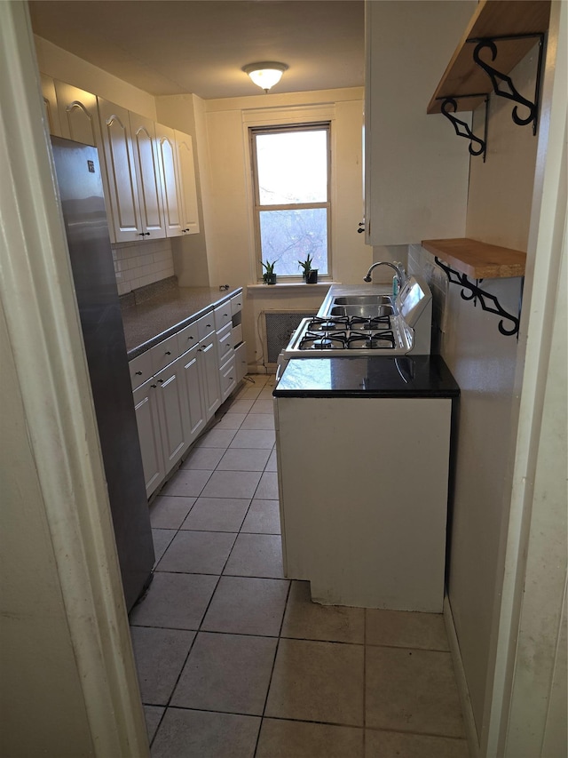 kitchen with light tile patterned floors, dark countertops, decorative backsplash, freestanding refrigerator, and a sink