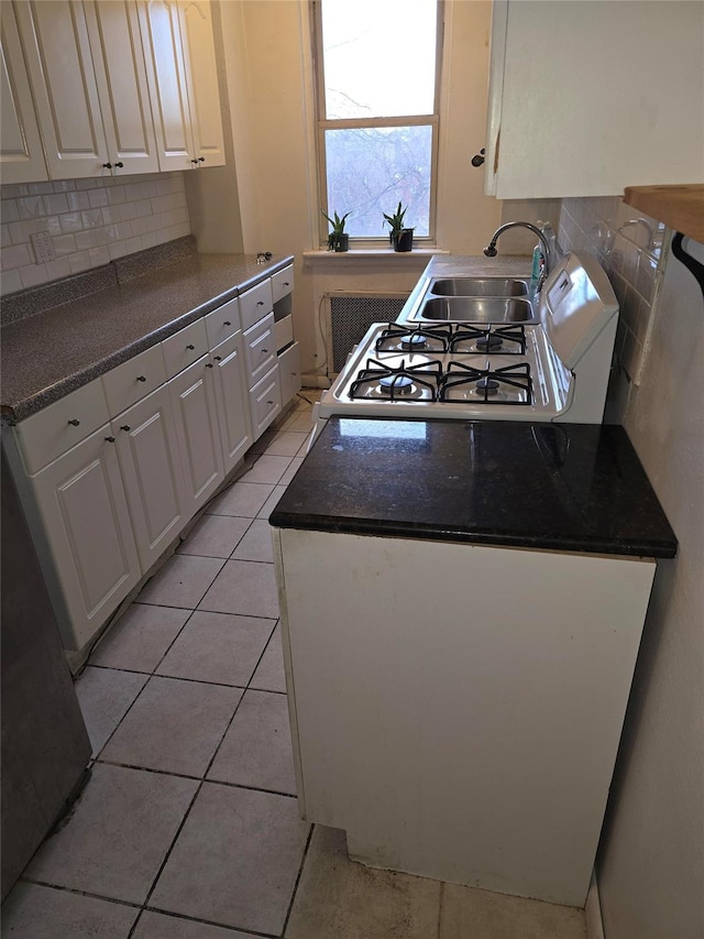 kitchen with white gas stove, tasteful backsplash, white cabinets, a sink, and light tile patterned flooring