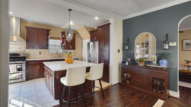 kitchen with stainless steel appliances, light countertops, wall chimney range hood, a kitchen bar, and a sink