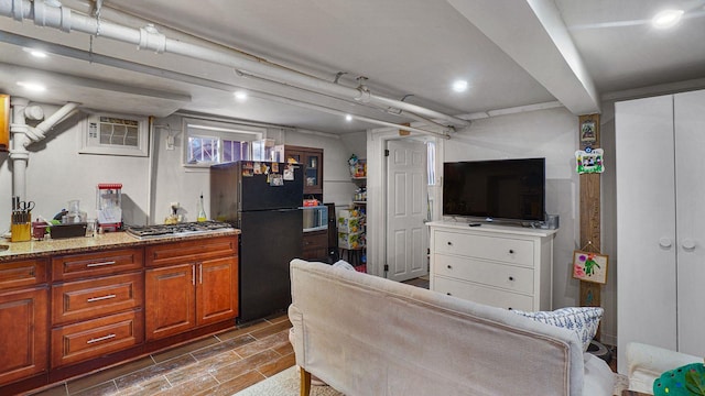 kitchen with appliances with stainless steel finishes, brown cabinets, light stone counters, wood finish floors, and a wall mounted AC