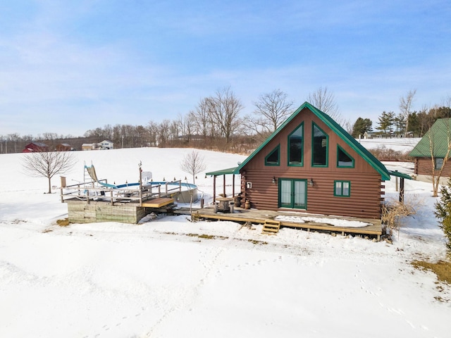 snow covered back of property with french doors, a deck, and log siding