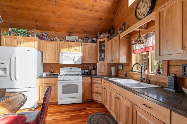 kitchen featuring lofted ceiling, white appliances, wood finished floors, a sink, and dark countertops