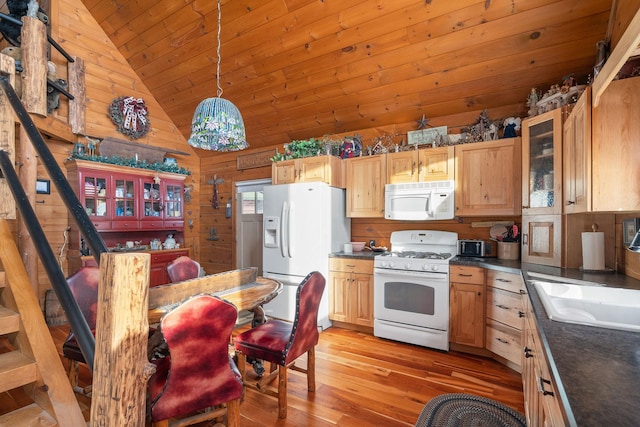 kitchen with dark countertops, lofted ceiling, a sink, wooden walls, and white appliances