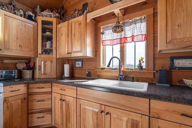 kitchen with dark countertops, wooden walls, glass insert cabinets, and a sink