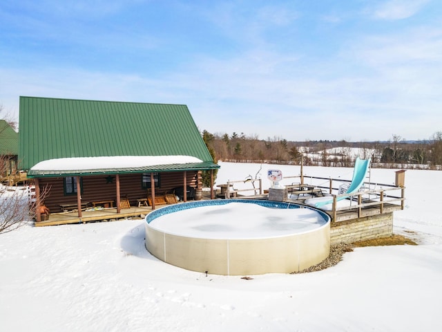 snow covered pool with a fenced in pool, a water slide, and a wooden deck