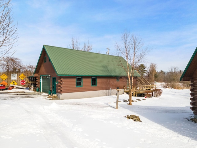 snow covered property with metal roof, a detached garage, and log siding