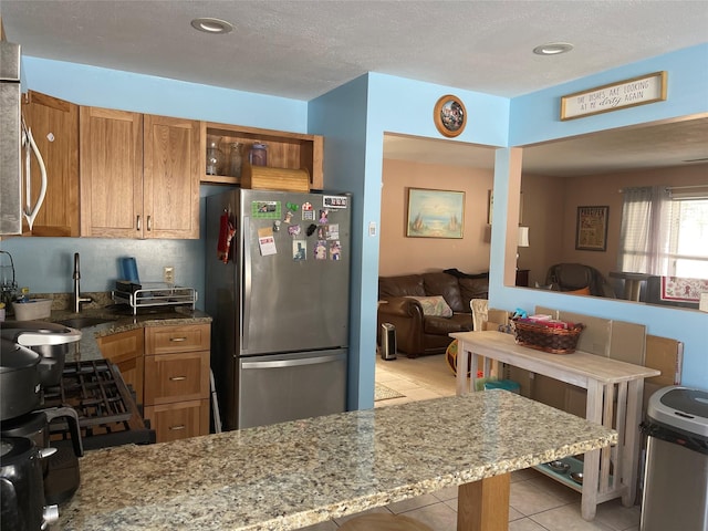 kitchen featuring light stone countertops, light tile patterned floors, brown cabinetry, and freestanding refrigerator