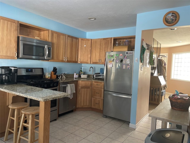 kitchen featuring appliances with stainless steel finishes, a sink, light stone counters, and open shelves