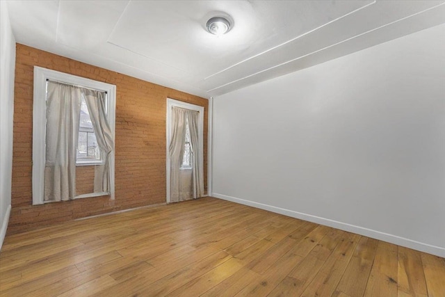 spare room with brick wall, light wood finished floors, and baseboards