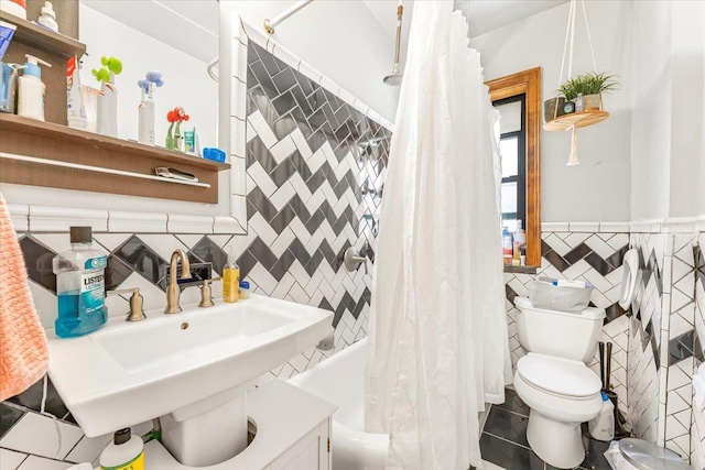 bathroom with a wainscoted wall, shower / tub combo with curtain, tile walls, toilet, and a sink