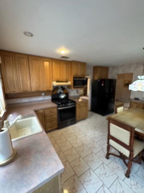 kitchen with marble finish floor, stove, freestanding refrigerator, a sink, and under cabinet range hood