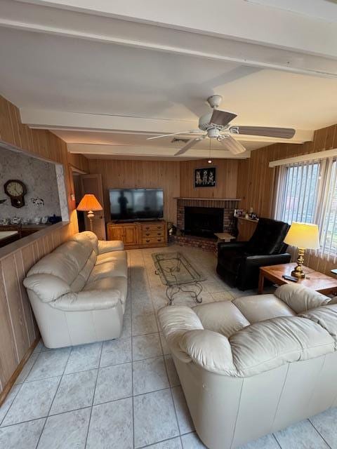 living area with a brick fireplace, light tile patterned flooring, ceiling fan, wooden walls, and beamed ceiling