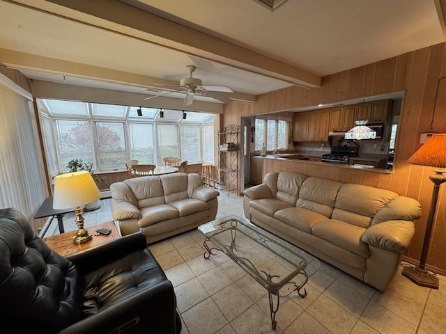 living room with light tile patterned floors, beamed ceiling, a ceiling fan, and wooden walls