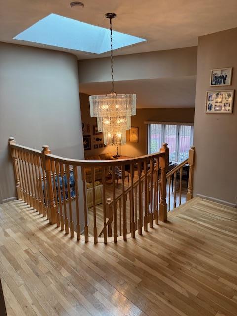 stairs with a skylight, wood-type flooring, and an inviting chandelier