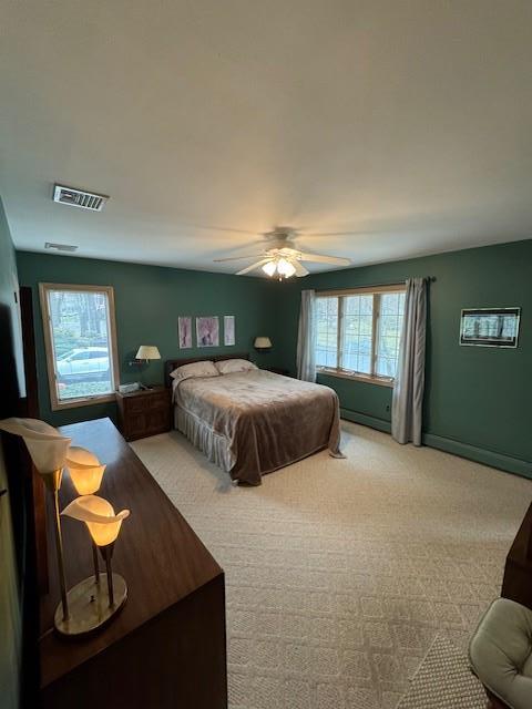 bedroom with multiple windows, visible vents, a ceiling fan, and light colored carpet