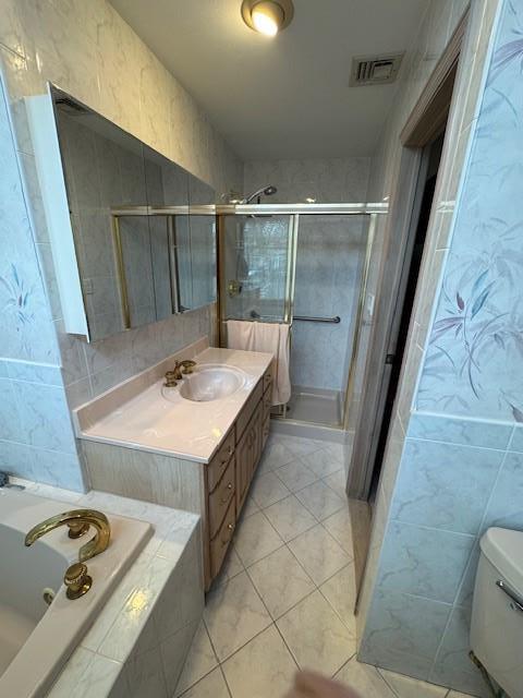 bathroom featuring a stall shower, a garden tub, visible vents, and tile walls